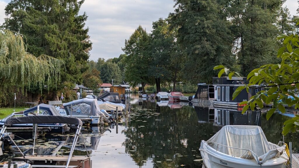 Kleine Boote und Hausboot an einem grünen Wasserweg in Rahnsdorf