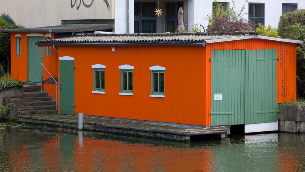 Orangefarbener Boots- und Waschschuppen mit grünen Türen am Wasser im Fischerkietz