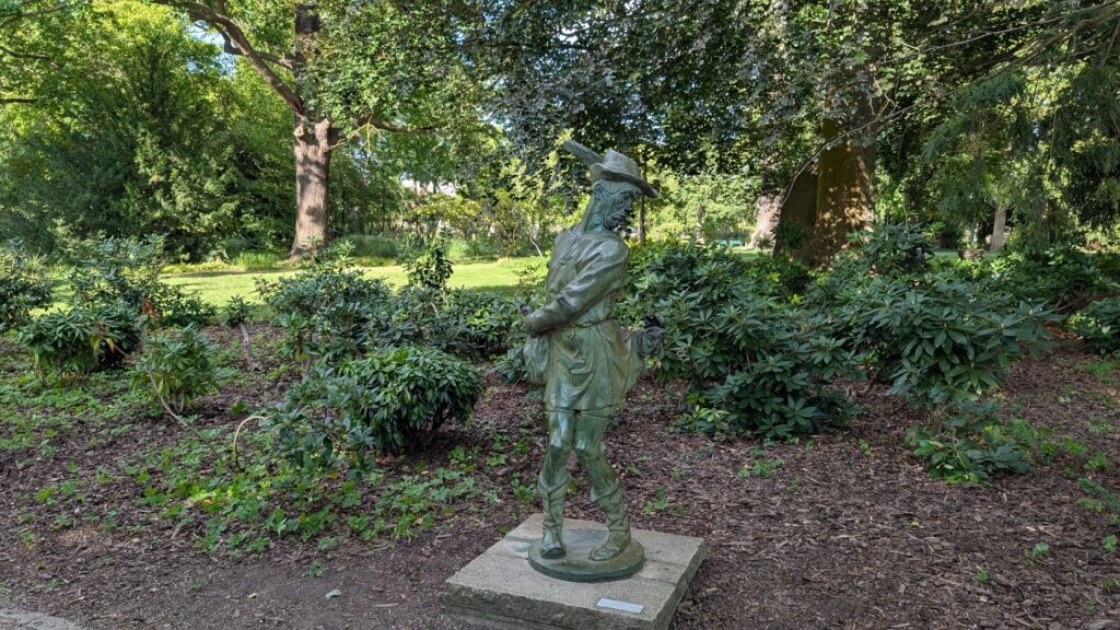 Jägerfigur im Schlosspark Köpenick zwischen Rhododendren und Bäumen