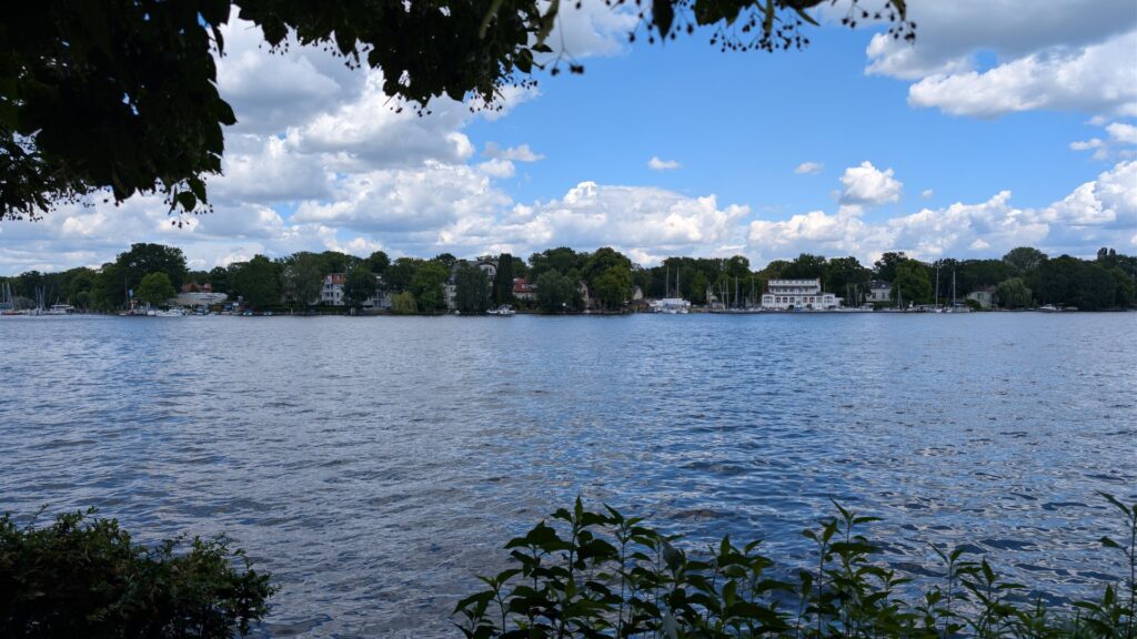 Blick über den Langen See bei Grünau mit ruhigem Wasser und grüner Uferkante.
