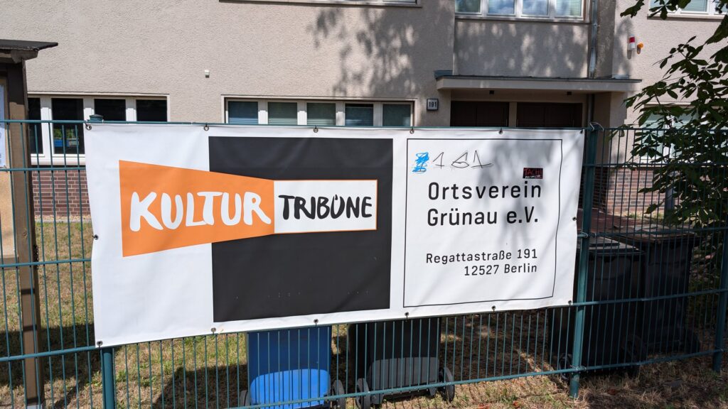 Schild der KulturTribüne und des Ortsvereins Grünau am Zaun.