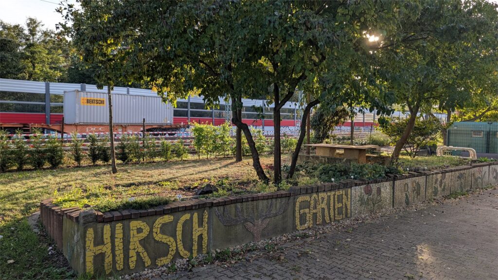 Gartenbereich der Gärtnerei Hirschgarten mit Bahnanlagen im Hintergrund