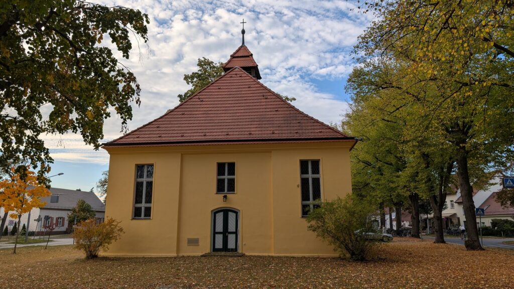 Frontansicht der Dorfkirche Müggelheim zwischen alten Bäumen