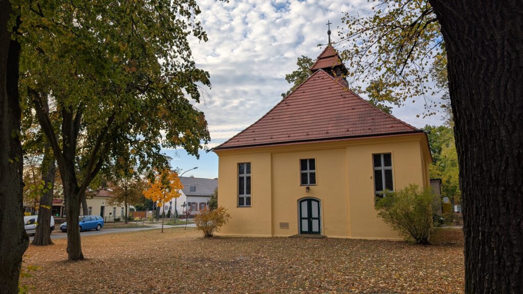 Dorfkirche Müggelheim mit herbstlichem Laub und Wolkenhimmel