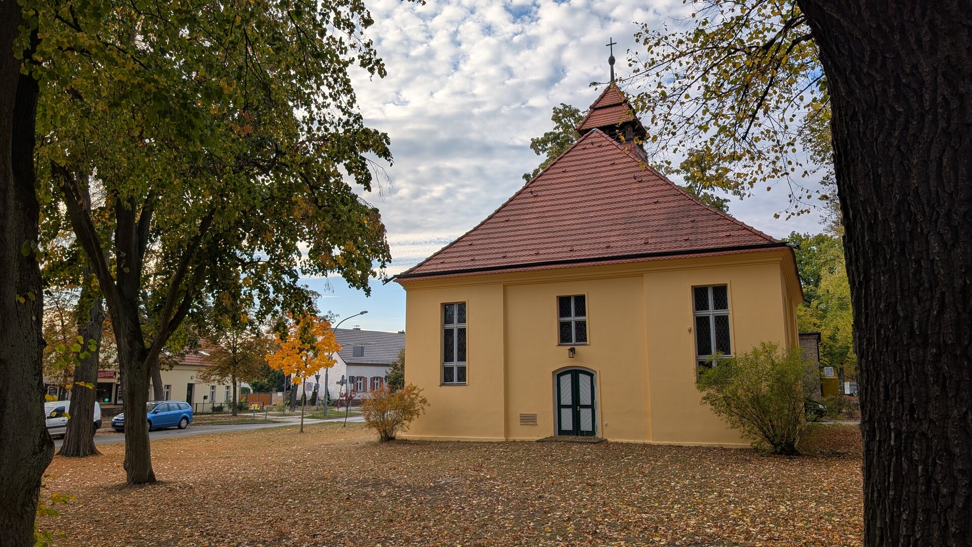 Dorfkirche Müggelheim mit herbstlichem Laub und Wolkenhimmel