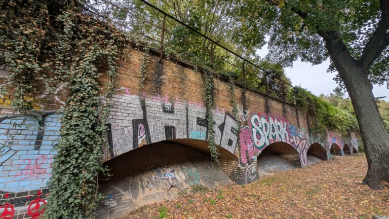 Bewachsener Bahndamm und Backsteinbögen an der Kiefholzstraße